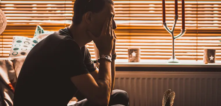 A man sitting with his hand over his face by a window