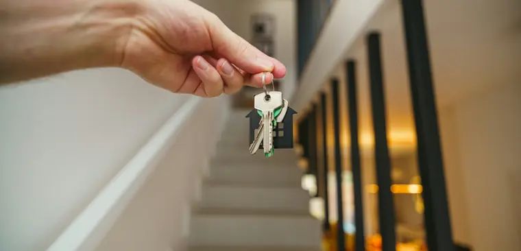 A hand holding a set of house keys in an empty hallway